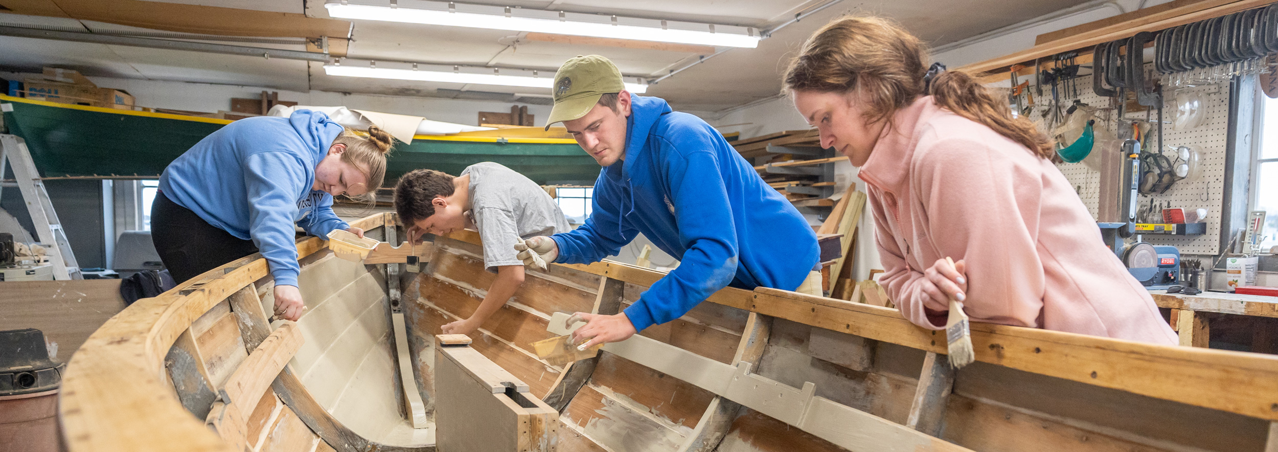 From left, UConn students Meghan Allmendingur, John Milczanowski and Aidan Davies – as well as Davies' sister, Sydney Davies – paint the interior of the boat Aidan is restoring for his capstone project in the John Gardner Boathouse at UConn Avery Point