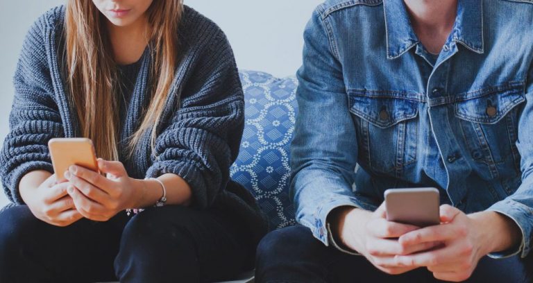 A man and woman, side by side, paying more attention to their phones than to each other, in what is known as "phubbing."