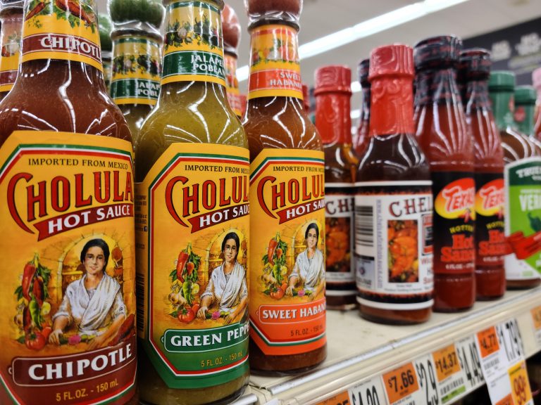Bottles of hot sauce lined up on a shelf in a super market.