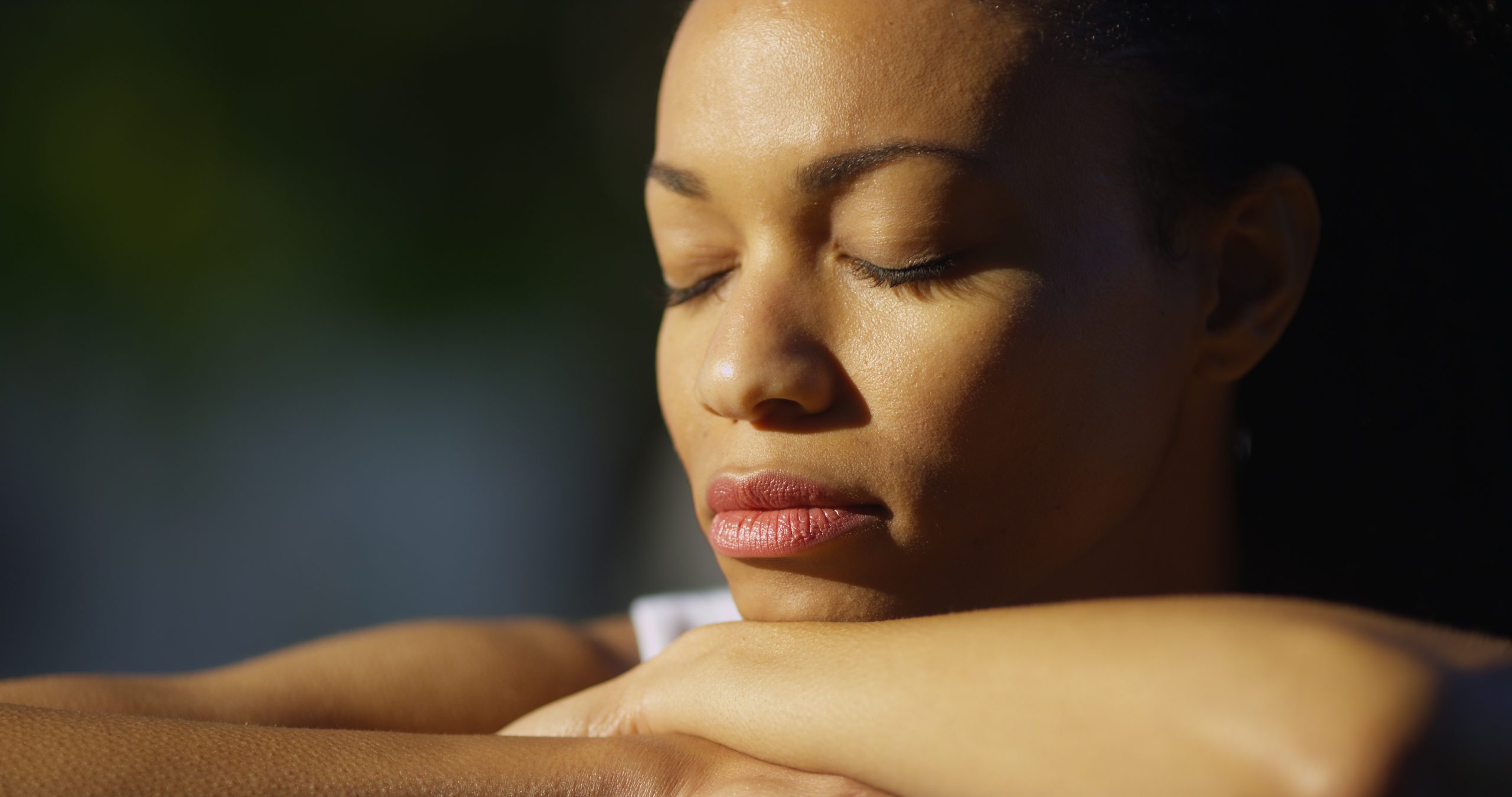 Black woman sitting with eyes closed outdoors.