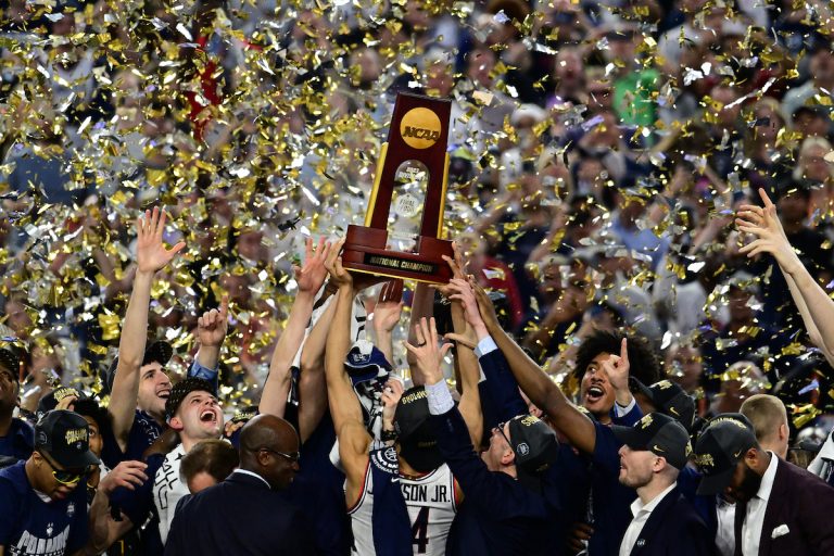 The UConn men's basketball team hold up the 2023 national championship trophy as confetti falls around them.