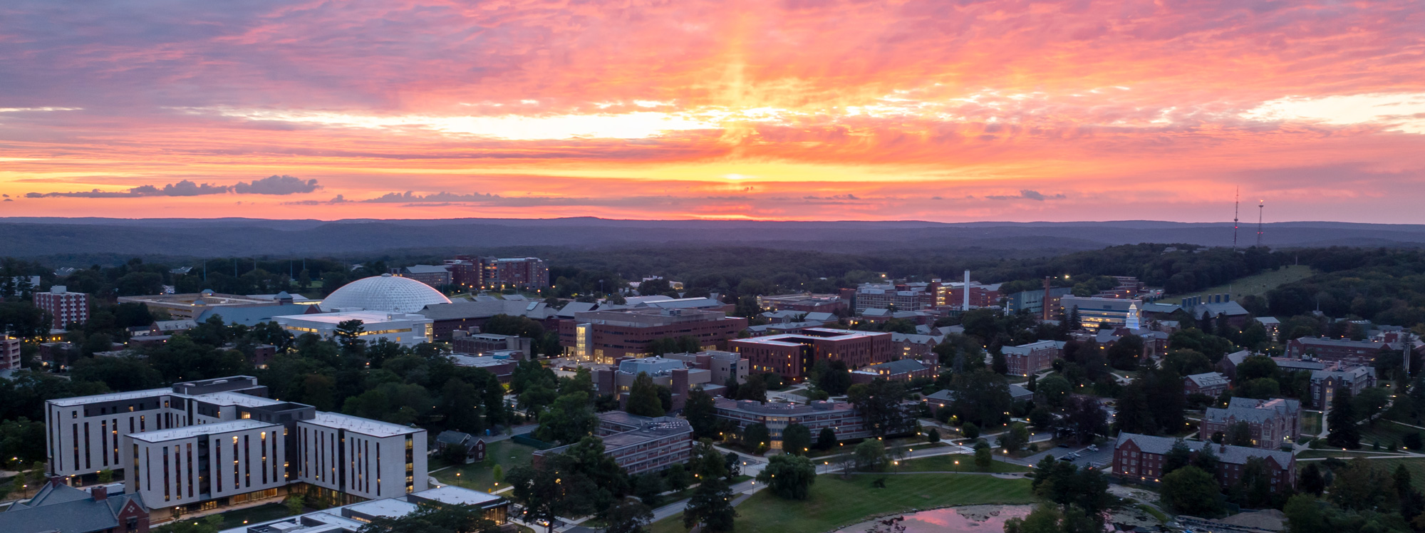 Sunset over a university campus with a white dome, modern and traditional buildings, and tree-lined paths.