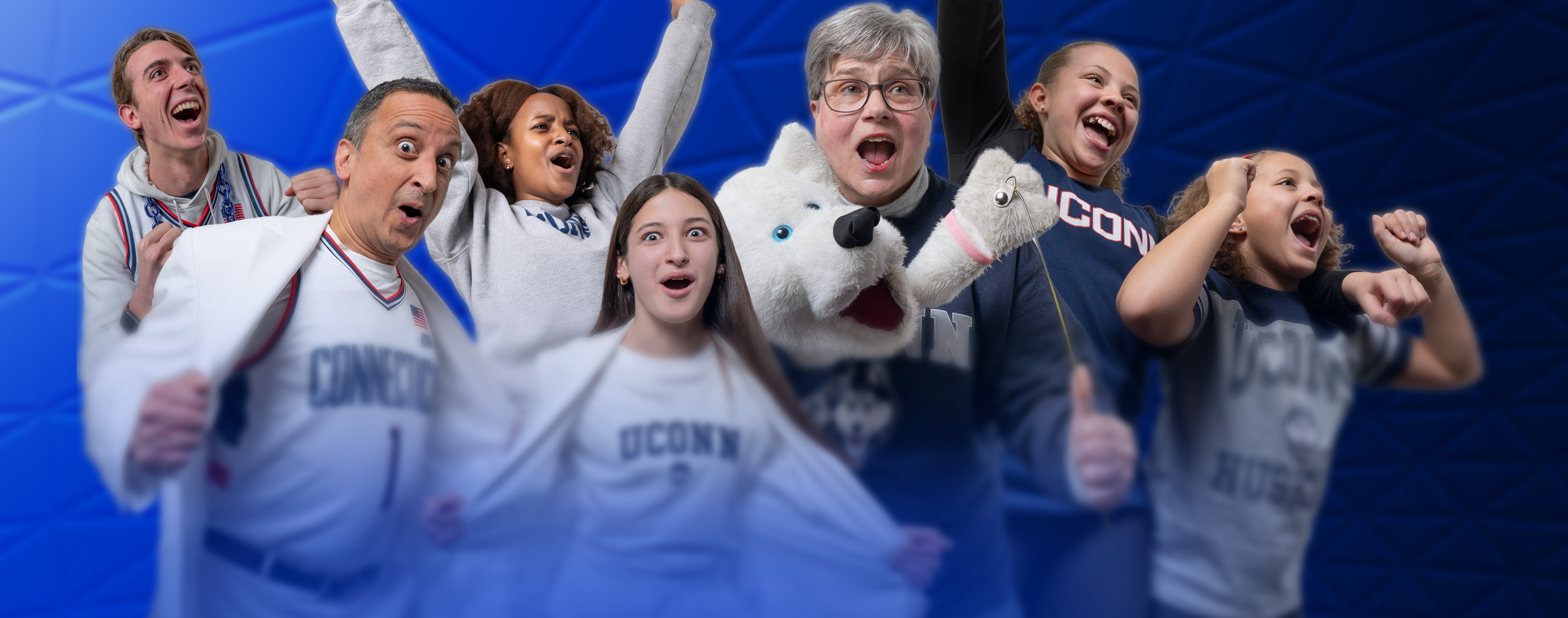 UConn fans and the Husky mascot celebrate together in front of a blue geometric backdrop, showing team spirit with UConn apparel and energetic poses.